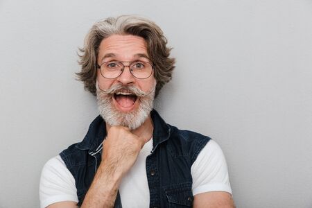 Portrait of a handsome excited stylish mature man wearing a vest standing isolated over gray background, screamingの写真素材