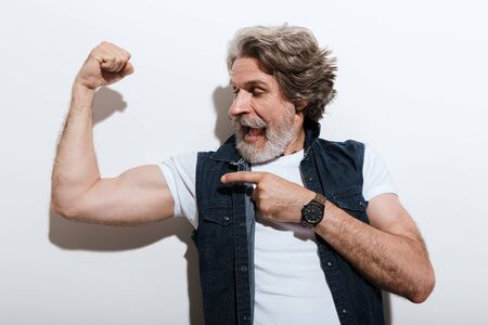 Portrait of a handsome stylish mature man wearing a vest standing isolated over gray background,...