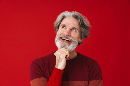 Portrait of happy old man wearing sweater smiling and looking upward isolated over red background