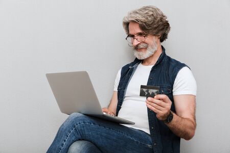 Portrait of a handsome smiling stylish mature man wearing a vest sitting on a chair isolated over...