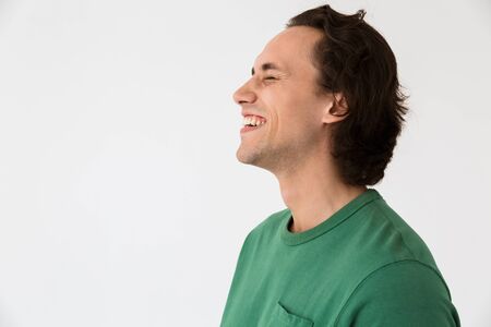 Image in profile of happy brunette man wearing basic t-shirt smiling by copyspace isolated over white backgroundの写真素材
