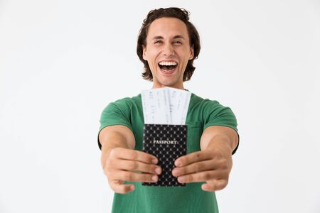 Image of attractive brunette man wearing basic t-shirt holding passport and travel tickets isolated...