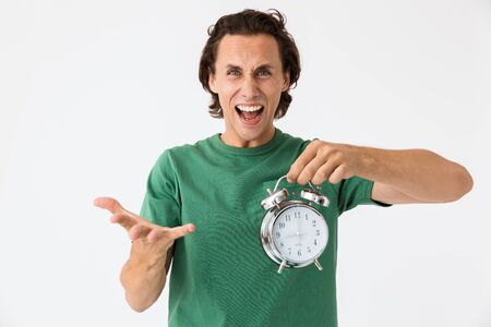 Image of shocked brunette man wearing basic t-shirt screaming and holding alarm clock isolated over...