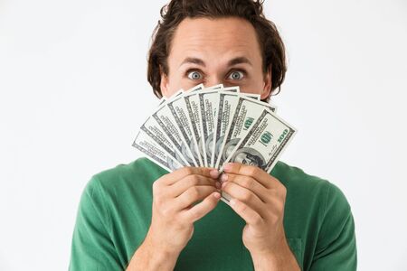 Image of positive brunette man wearing basic t-shirt covering his face with cash money isolated over...