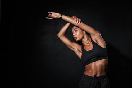 Confident fit young african fitness woman doing stretching exercises while standing isolated over...