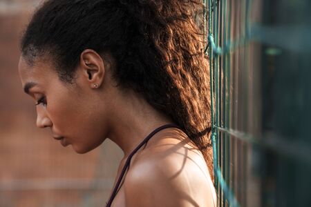 Photo in profile of african american nice woman in sportswear standing while working out at playground outdoorsの写真素材