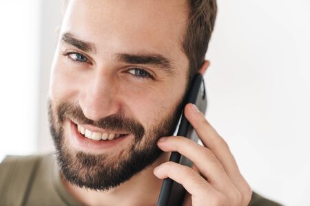 Image closeup of caucasian happy man talking on cellphone and smiling while working in bright officeの写真素材