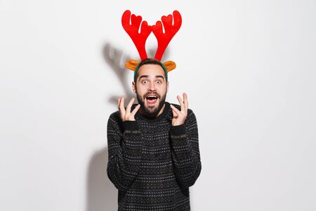 Image of excited young man in Christmas reindeer antlers headband screaming with delight isolated over gray backgroundの写真素材