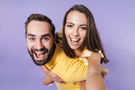 Happy excited beautiful young couple wearing casual clothing standing isolated over violet...