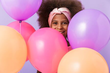 Image of a cute happy young african girl kid posing with balloons isolated over purple wall background.の写真素材