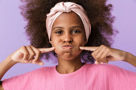 Image of a funny cute young african girl kid posing isolated over purple wall background having fun.の写真素材