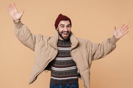 Portrait of a happy young bearded man wearing winter jacket standing isolated over beige
