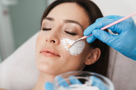 Photo of relaxed caucasian woman getting cosmetic procedure by specialist while lying in beauty...