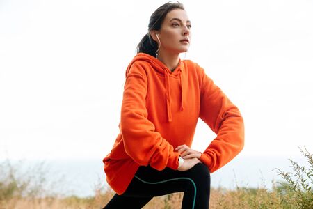 Photo of nice athletic woman in sportswear using earphones and doing exercise while working out at seashoreの写真素材
