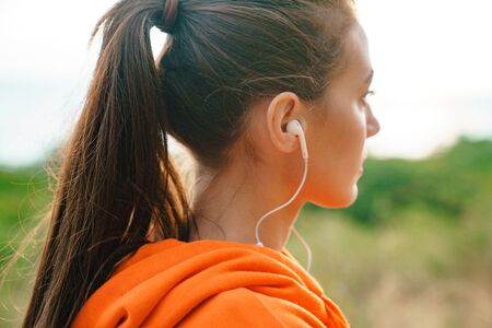 Photo of beautiful athletic woman in sportswear using earphones while working out at seashore