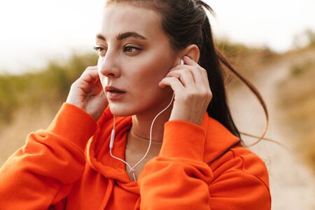 Photo of beautiful athletic woman in sportswear using earphones while working out at seashoreの写真素材