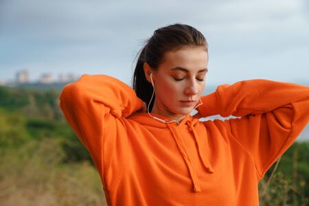 Photo of beautiful brunette woman in sportswear using earphones while working out at seashore