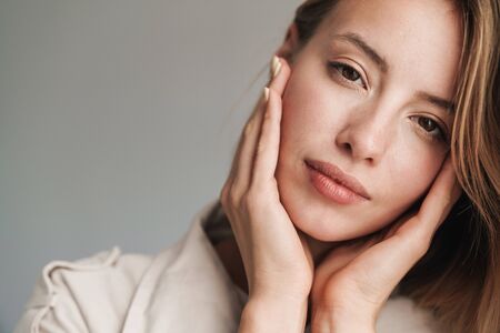 Close up of a lovely young blonde short haired woman leaning on a wall indoors, looking at camera