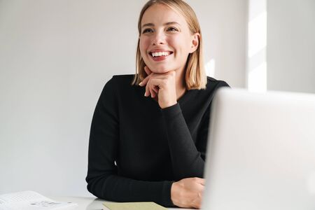 Confident smiling attractive young business woman sitting at the desk while working at the office on...