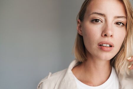 Close up of a lovely young blonde short haired woman leaning on a wall indoors, looking at camera