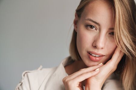 Close up of a lovely young blonde short haired woman leaning on a wall indoors, looking at camera