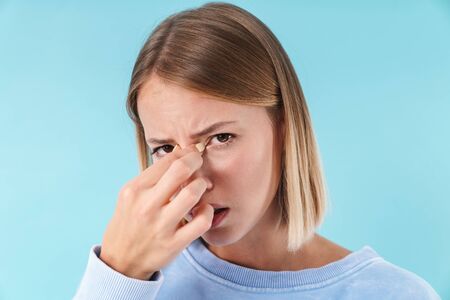 Portrait of a beautiful upset young blonde short haired woman wearing sweatshirt standing isolated over blue background, suffering from a headacheの写真素材