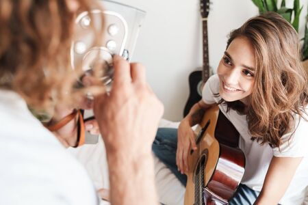 Photo of a cheery happy young loving couple indoors at home play on guitar.