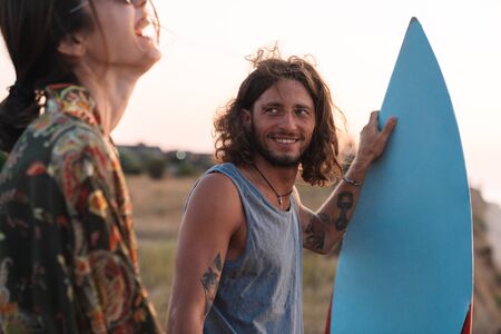 Happy young couple holding while standing at the beach, holding surf board
