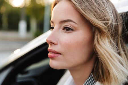Image of young caucasian beautiful businesslike woman sitting in luxury car outdoorsの写真素材