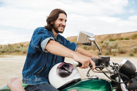 Image of a handsome smiling cheerful optimistic man biker on his bike outdoors on a beach.
