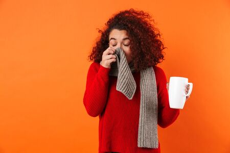 Image of a sick young sneeze woman posing isolated over orange background holding cup of hot tea...