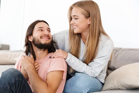 Image of optimistic smiling young loving couple on sofa watch tv film indoors at home hugging.