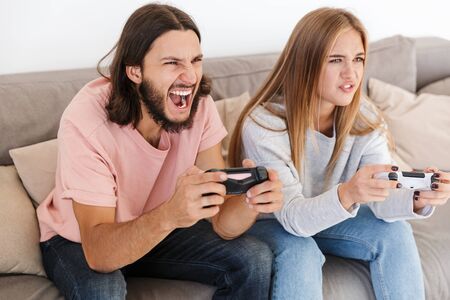 Photo of nervous young loving couple on sofa play video games with joystick indoors at home.
