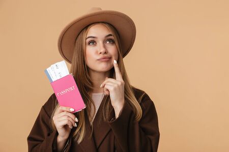 Image of young optimistic girl wearing hat holding passport and travel tickets isolated over beige backgroundの写真素材