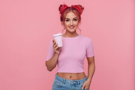 Portrait of happy woman with colorful hairstyle smiling and holding takeaway coffee cup isolated over pink backgroundの写真素材