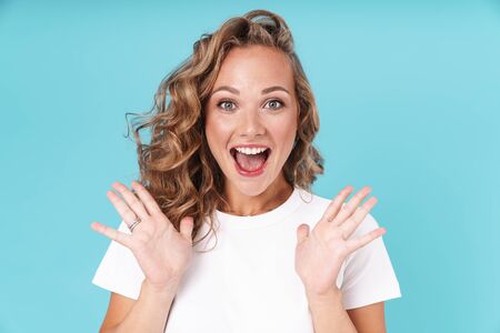 Attractive excited young girl wearing casual clothing standing isolated over blue background, celebrating successの写真素材