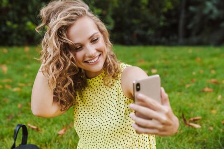 Photo of a young pretty pleased woman outdoors in nature park take a selfie by mobile phone.の写真素材