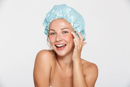 Image of happy woman wearing cosmetic patches and shower cap smiling isolated over white backgroundの写真素材