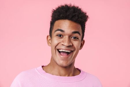 Portrait of a smiling african teenager boy wearing pullower standing isolated over pink background, looking at cameraの写真素材
