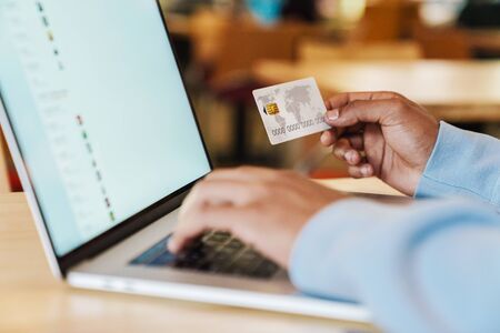 Close up of a businessman working on laptop computer indoors, holding credit cardの写真素材