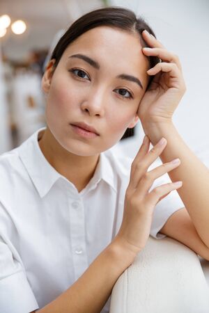 Attractive young asian businesswoman leaning on a couch while sitting at the cafe indoorsの写真素材