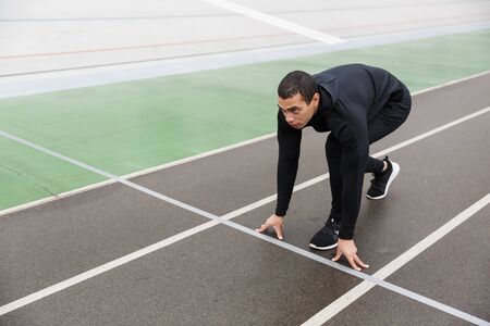 Photo of athletic strong sportsman in tracksuit doing exercise while working out on stadium after...