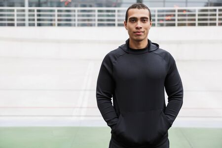 Photo of athletic caucasian sportsman in tracksuit standing and looking at camera while working out on stadium after rainの写真素材
