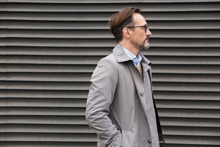 Image in profile of handsome bearded businessman in eyeglasses looking forward while standing near...