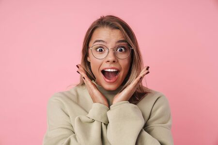 Portrait of young delighted woman in eyeglasses smiling and looking at camera isolated over pink backgroundの写真素材