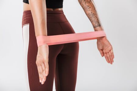 Cropped image of young woman in sportswear doing workout with expander equipment isolated over white...