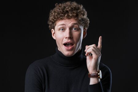 Excited young man wearing turtleneck standing isolated infront of a black background, pointing away