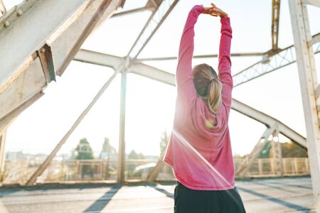 Back view image of a beautiful amazing young sports fitness woman make stretching exercises outdoors.の写真素材