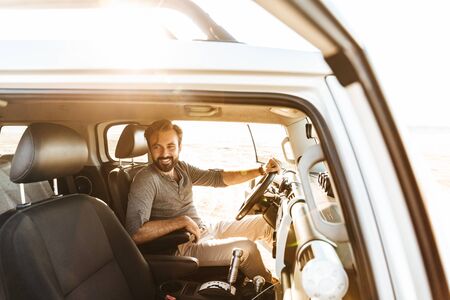 Image of handsome positive young man drive the car outdoors at the beach.の写真素材