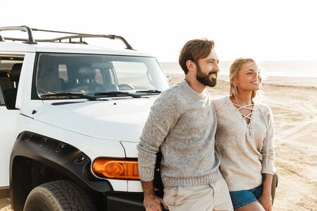 Photo of young pleased smiling happy loving couple outdoors at beach near car.